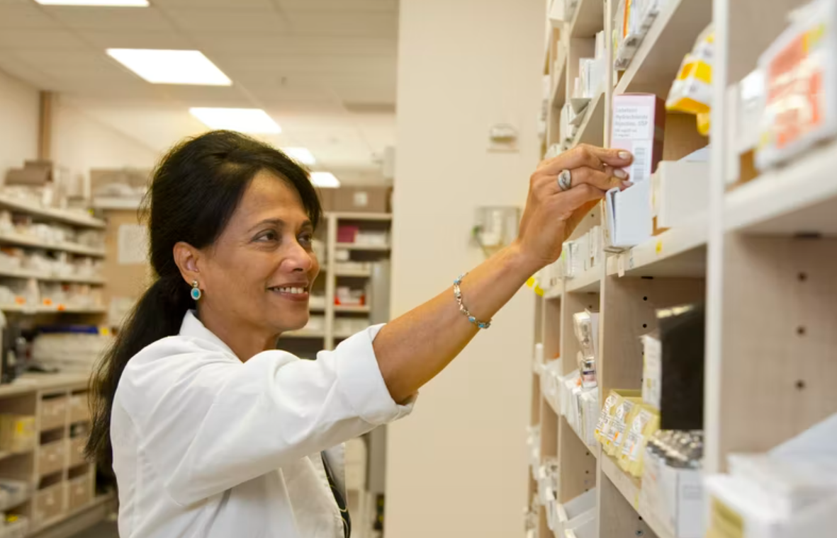 A woman in the pharmaceutical industry reaches for a prescription medication on the shelf in a pharmac