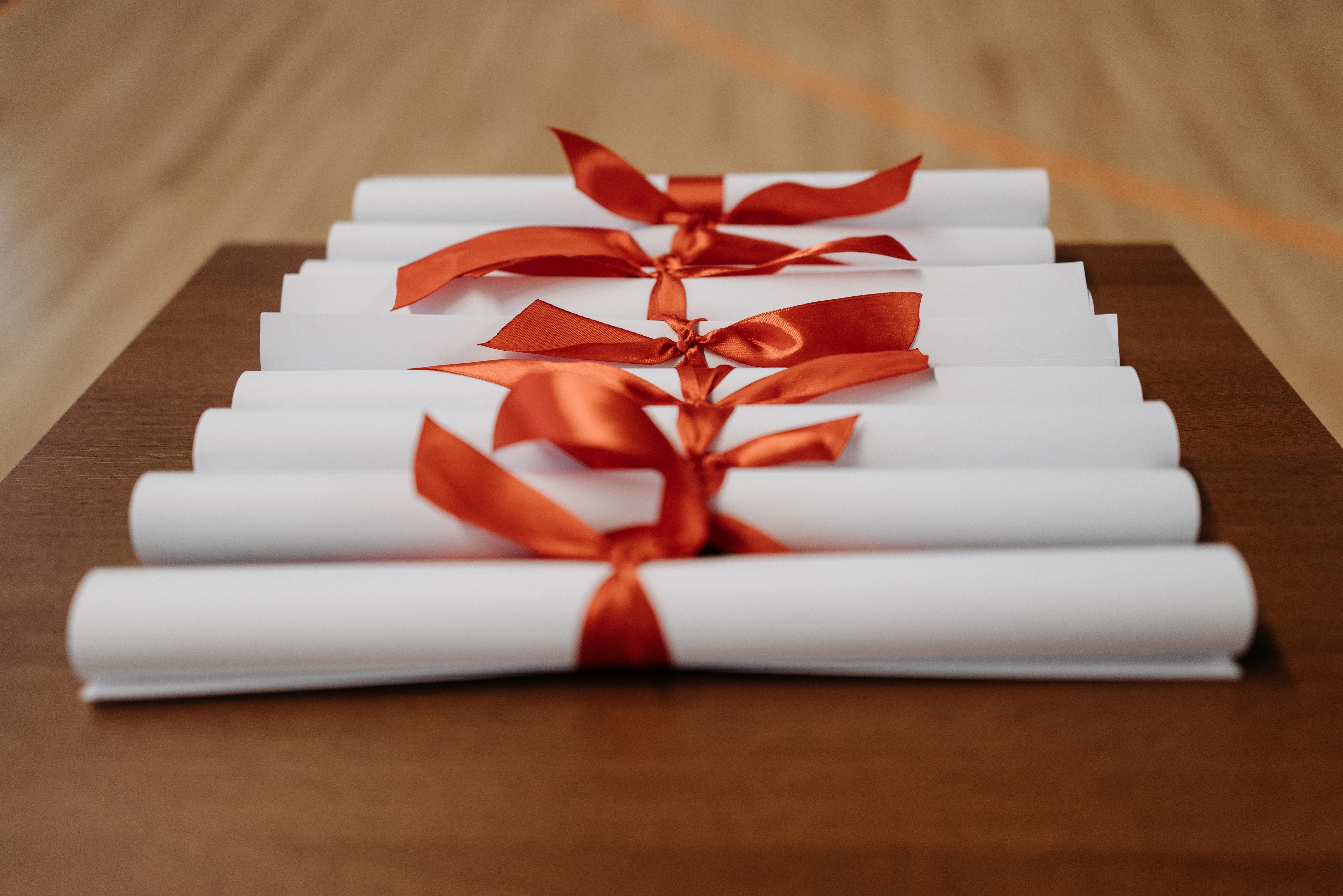 Paper scrolls representing higher diplomas are lined up on a wooden table